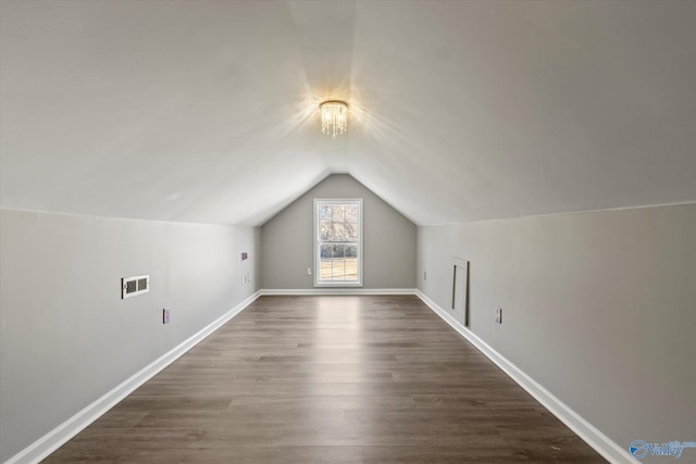 bonus room featuring a notable chandelier, lofted ceiling, and dark wood-type flooring