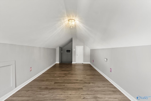 additional living space featuring a chandelier, lofted ceiling, and dark wood-type flooring