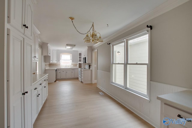 kitchen with light hardwood / wood-style floors, white cabinetry, decorative light fixtures, a chandelier, and crown molding