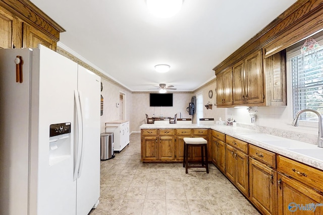 kitchen with white fridge with ice dispenser, kitchen peninsula, ceiling fan, ornamental molding, and sink