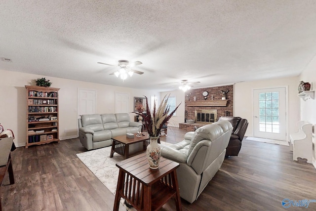 living room with a brick fireplace, a textured ceiling, ceiling fan, and dark wood-type flooring