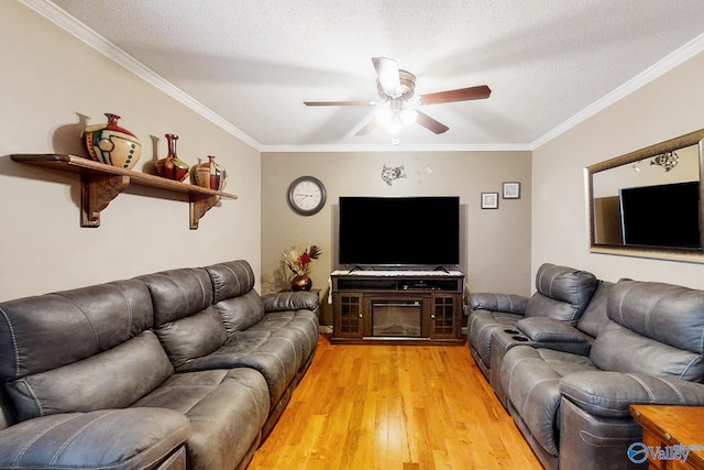 living room featuring a textured ceiling, a fireplace, ornamental molding, light wood-type flooring, and ceiling fan