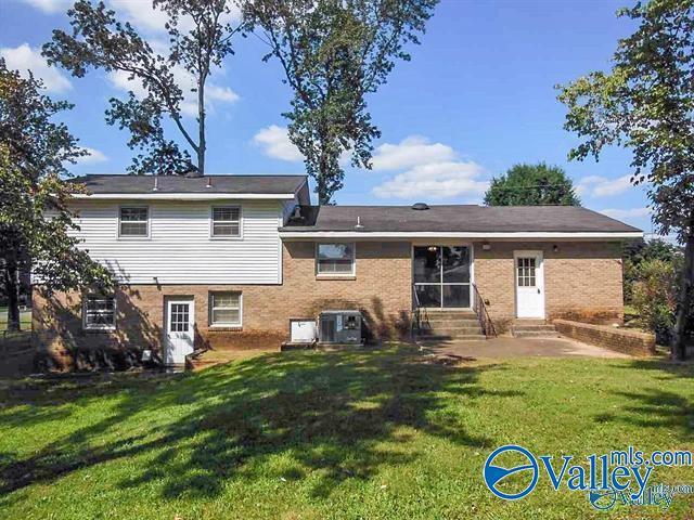 back of property with entry steps, central AC, a lawn, and brick siding