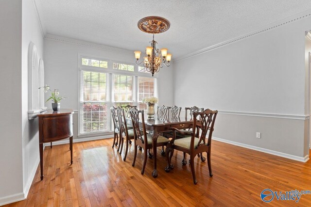dining room featuring light wood-type flooring, a textured ceiling, crown molding, and an inviting chandelier
