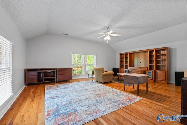 interior space featuring vaulted ceiling, visible vents, a ceiling fan, light wood-style floors, and a textured ceiling