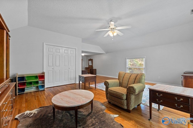 living area with lofted ceiling, wood finished floors, baseboards, a textured ceiling, and ceiling fan