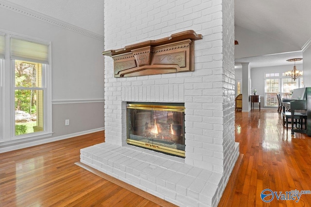 interior details featuring wood finished floors, a brick fireplace, baseboards, and an inviting chandelier