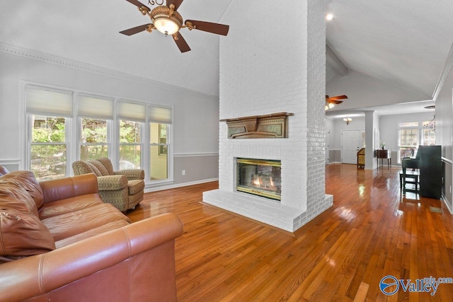 living area featuring a ceiling fan, wood-type flooring, baseboards, a brick fireplace, and high vaulted ceiling