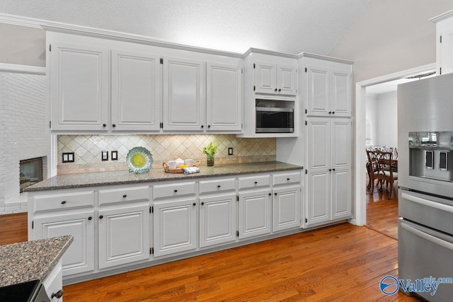 kitchen with light wood finished floors, light stone counters, decorative backsplash, stainless steel fridge, and white cabinetry