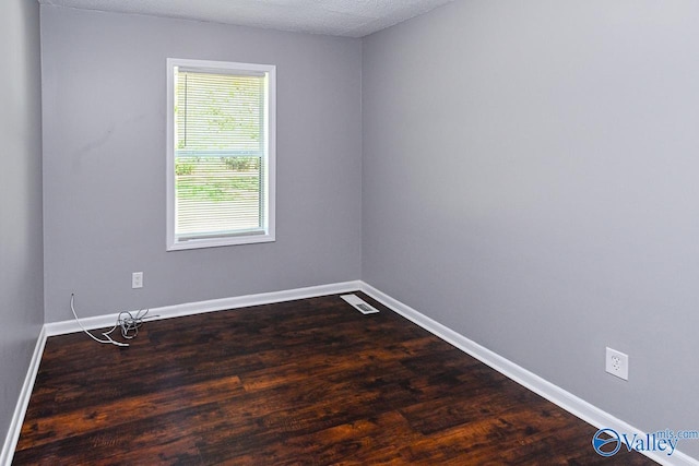 empty room featuring a textured ceiling and dark hardwood / wood-style flooring