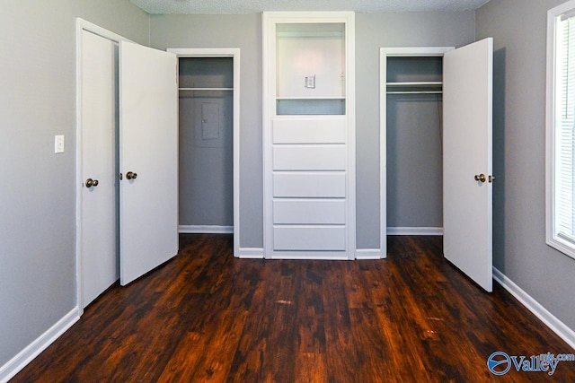 unfurnished bedroom featuring a textured ceiling, multiple closets, and dark wood-type flooring