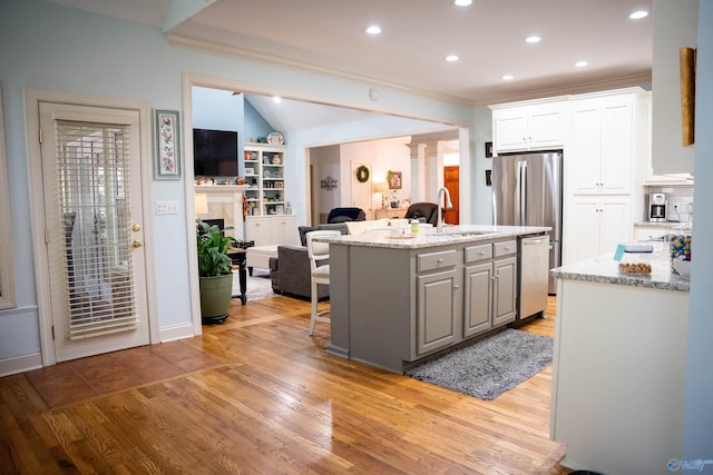 kitchen with an island with sink, sink, light hardwood / wood-style flooring, appliances with stainless steel finishes, and a breakfast bar