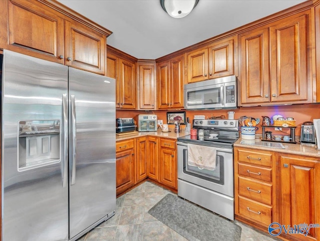 kitchen featuring stainless steel appliances, brown cabinetry, and light tile patterned floors