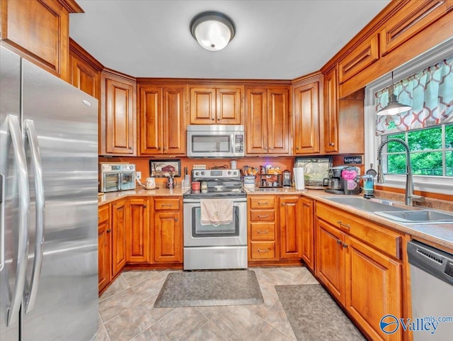kitchen featuring stainless steel appliances, a sink, brown cabinets, and light countertops