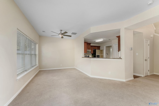 unfurnished living room featuring sink, light carpet, and ceiling fan