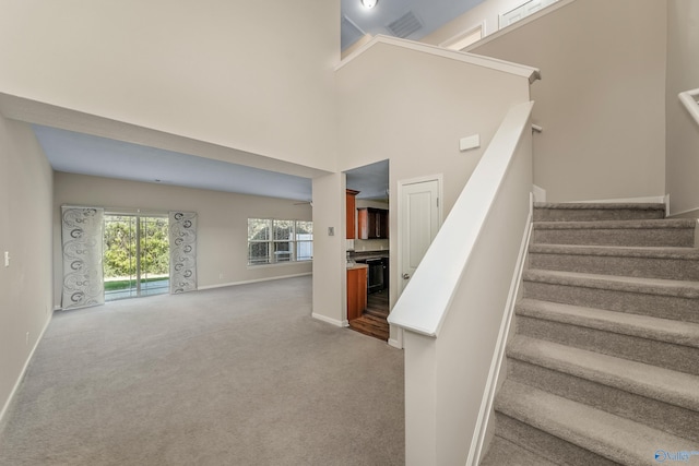 stairs with a towering ceiling, carpet floors, and ceiling fan