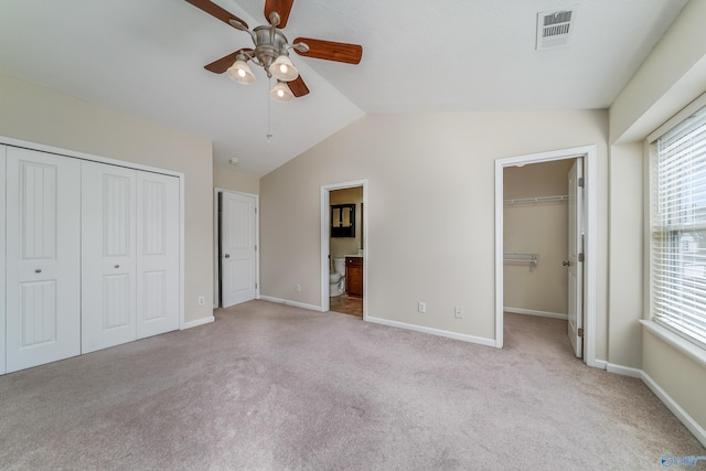 unfurnished bedroom featuring ceiling fan, ensuite bath, vaulted ceiling, and light colored carpet