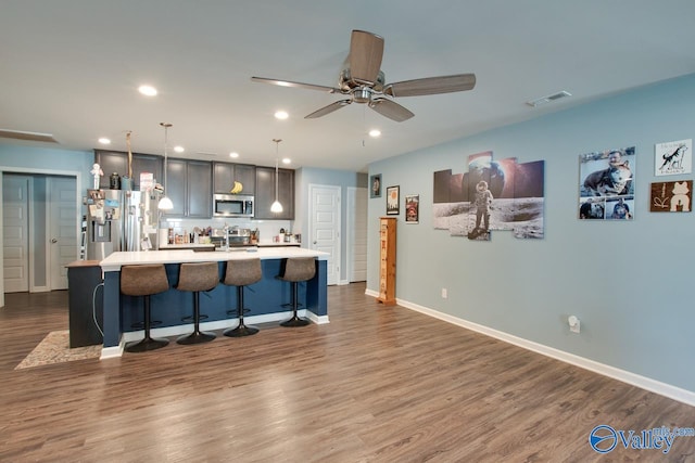 kitchen featuring a center island with sink, appliances with stainless steel finishes, decorative light fixtures, a kitchen bar, and dark hardwood / wood-style floors