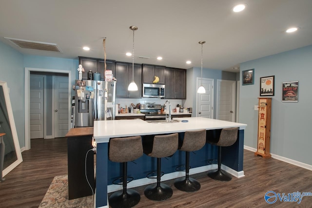 kitchen with stainless steel appliances, dark hardwood / wood-style floors, a center island with sink, and pendant lighting