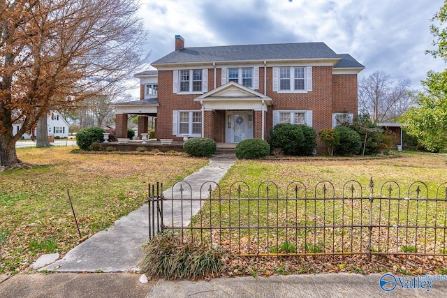 colonial inspired home with a fenced front yard, brick siding, a chimney, and a front lawn