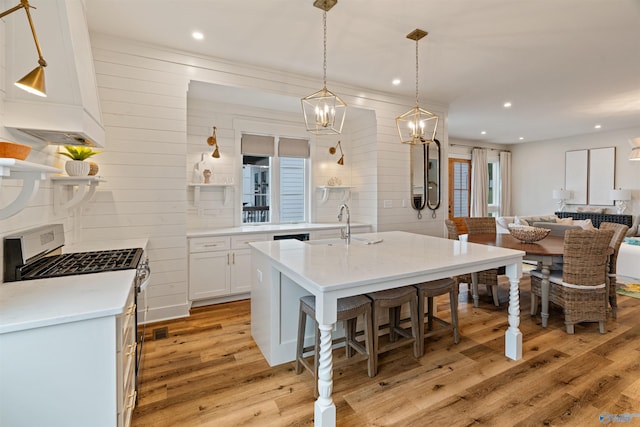 kitchen featuring light wood finished floors, light countertops, white cabinets, gas range, and a kitchen breakfast bar