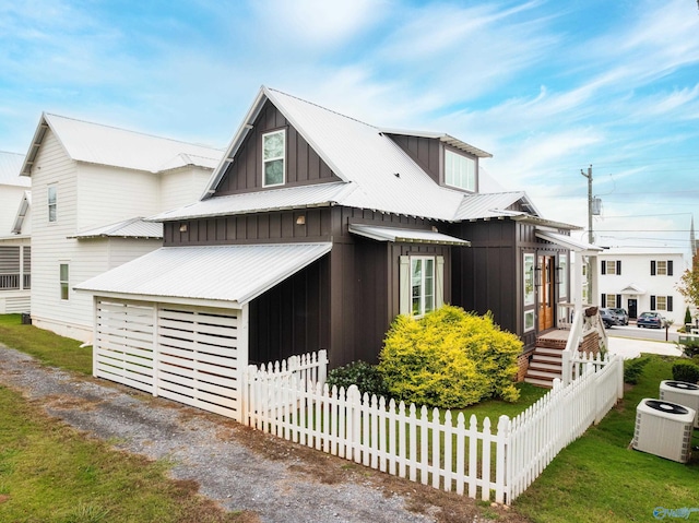 view of front of property featuring a front lawn, fence, cooling unit, board and batten siding, and metal roof