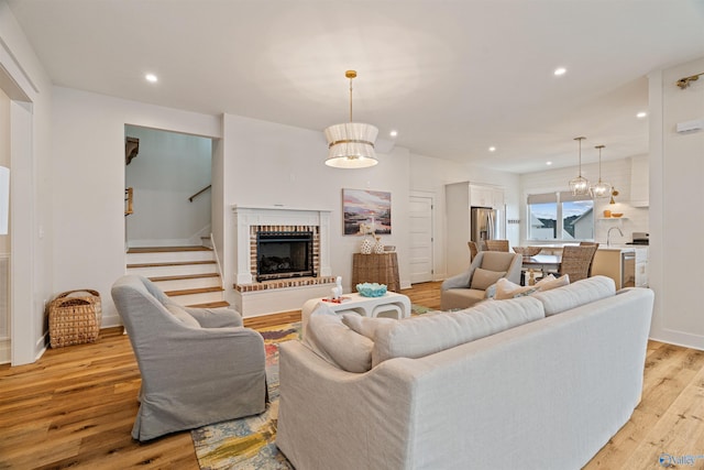 living room with recessed lighting, light wood finished floors, baseboards, a brick fireplace, and stairs