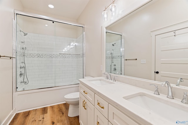 bathroom with a sink, toilet, wood finished floors, and combined bath / shower with glass door