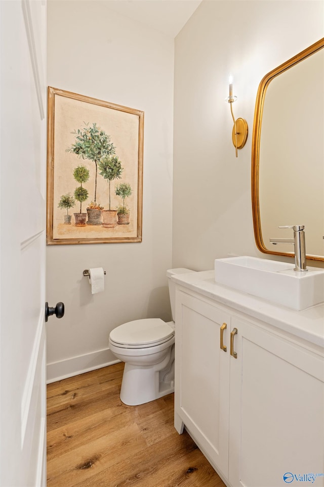 half bath with vanity, toilet, wood finished floors, and baseboards
