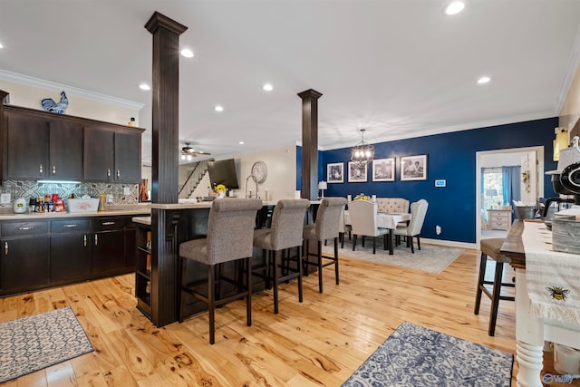 kitchen with ornate columns, dark brown cabinetry, ceiling fan, crown molding, and light hardwood / wood-style flooring