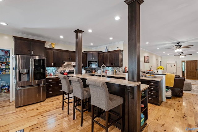 kitchen with appliances with stainless steel finishes, light hardwood / wood-style floors, ornate columns, and dark brown cabinets