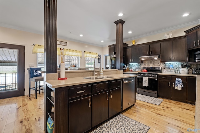 kitchen featuring sink, light hardwood / wood-style flooring, an island with sink, stainless steel appliances, and decorative columns