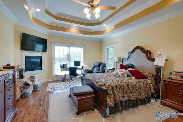 bedroom with light hardwood / wood-style flooring, ceiling fan, a tray ceiling, and crown molding