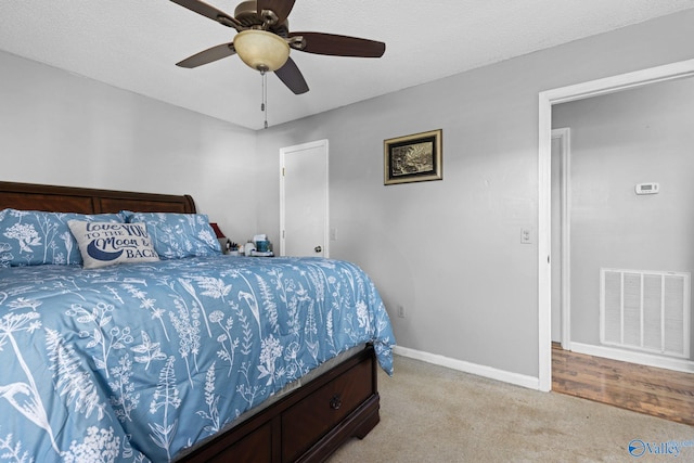 bedroom with ceiling fan, light colored carpet, and a textured ceiling