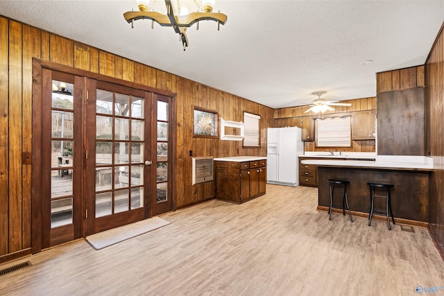 kitchen featuring heating unit, white fridge with ice dispenser, wood walls, and light wood-type flooring