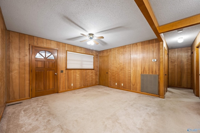 empty room featuring a textured ceiling, light colored carpet, ceiling fan, and wood walls