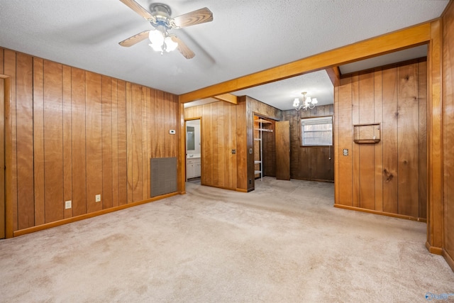 carpeted spare room with ceiling fan with notable chandelier, beam ceiling, and wood walls