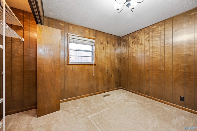 unfurnished room with wooden walls, light colored carpet, and a textured ceiling