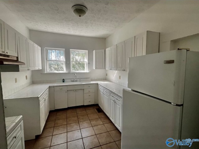 kitchen with white cabinets, a textured ceiling, light tile patterned floors, and white refrigerator