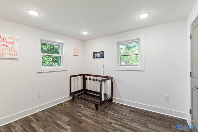 bedroom with dark wood-type flooring, multiple windows, and a crib