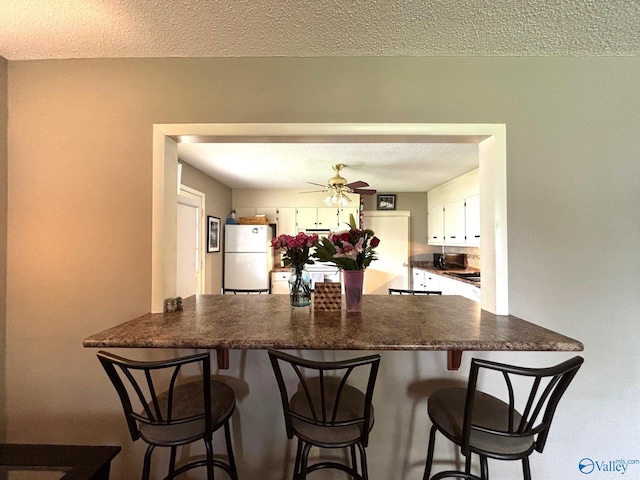 1300 7th Ave, Athens, AL 35611 - kitchen featuring freestanding refrigerator, a peninsula, dark countertops, white cabinets, and a textured ceiling