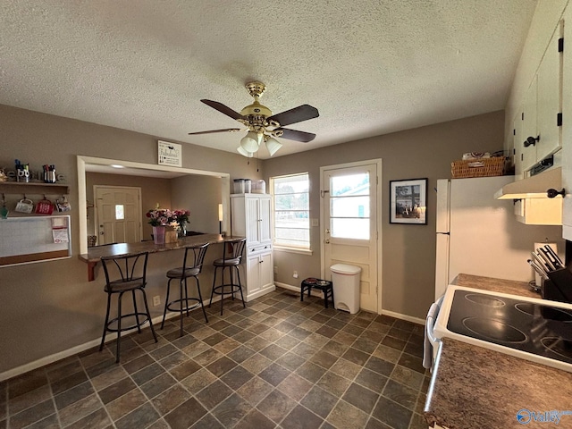 1300 7th Ave, Athens, AL 35611 - kitchen with ceiling fan, under cabinet range hood, a textured ceiling, a breakfast bar, and baseboards
