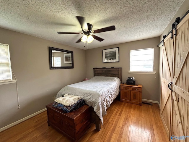 1300 7th Ave, Athens, AL 35611 - bedroom with a barn door, light wood-style floors, baseboards, a textured ceiling, and a ceiling fan