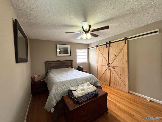 1300 7th Ave, Athens, AL 35611 - bedroom featuring a barn door, light wood-style floors, baseboards, a textured ceiling, and a ceiling fan