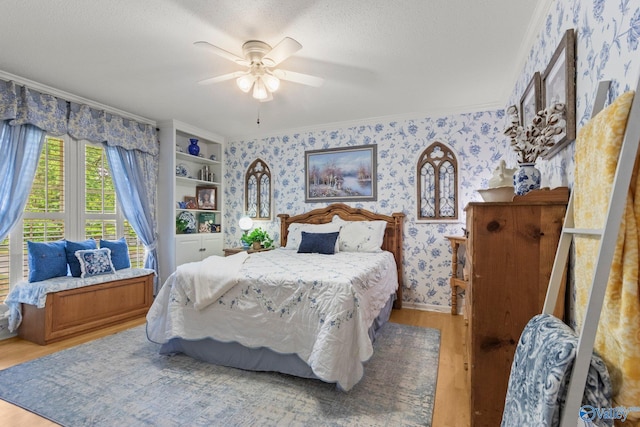 bedroom featuring wood finished floors, a ceiling fan, ornamental molding, and wallpapered walls