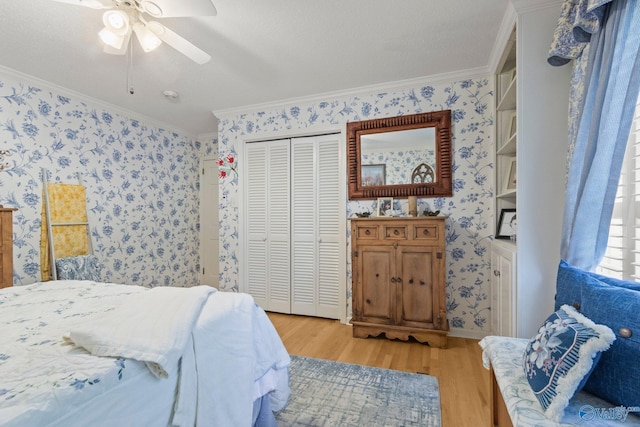 bedroom featuring a closet, crown molding, a ceiling fan, light wood-style flooring, and wallpapered walls