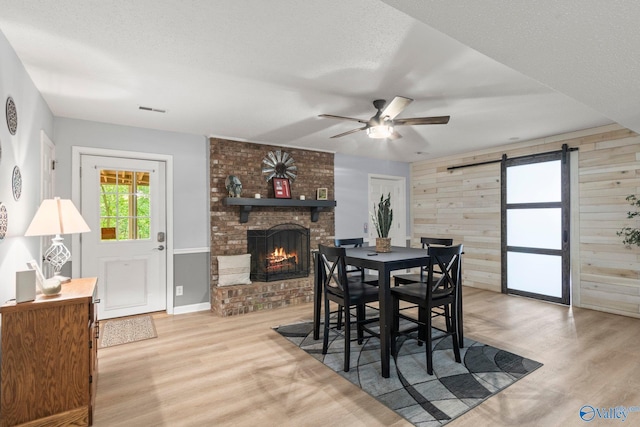dining room featuring wood walls, a barn door, light wood finished floors, a fireplace, and a ceiling fan