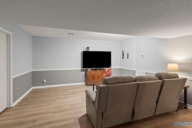 living room featuring a textured ceiling, light wood-style flooring, and baseboards
