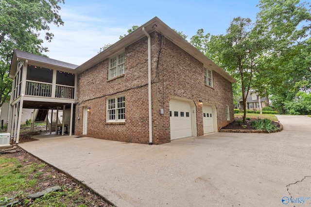 view of side of home featuring a sunroom, stairs, brick siding, concrete driveway, and an attached garage