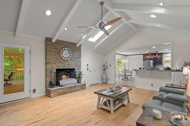 living room featuring light wood-style flooring, beamed ceiling, ceiling fan, a stone fireplace, and high vaulted ceiling